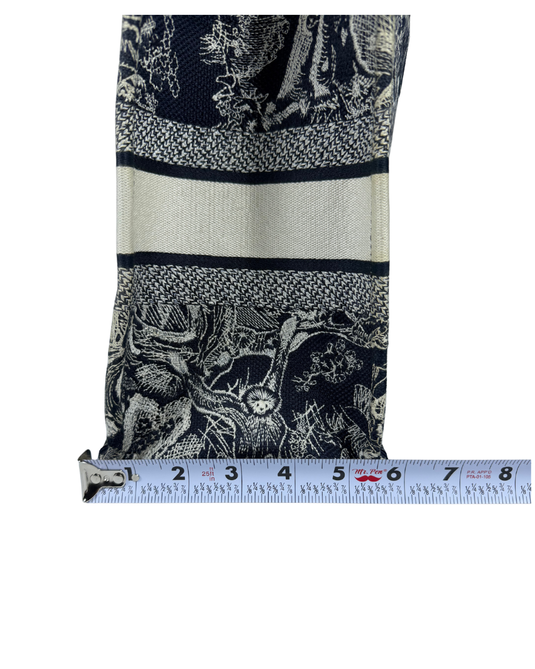A close-up of a patterned fabric panel with a navy blue and off-white toile-style print, shown next to a measuring tape to indicate scale, on a plain white background.
