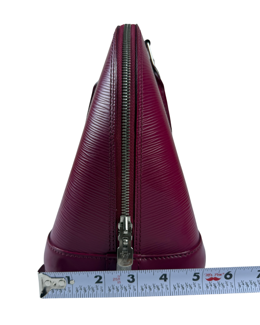 A close-up side view of a burgundy textured leather handbag with a silver zipper, shown next to a measuring tape to indicate its size, on a white background.