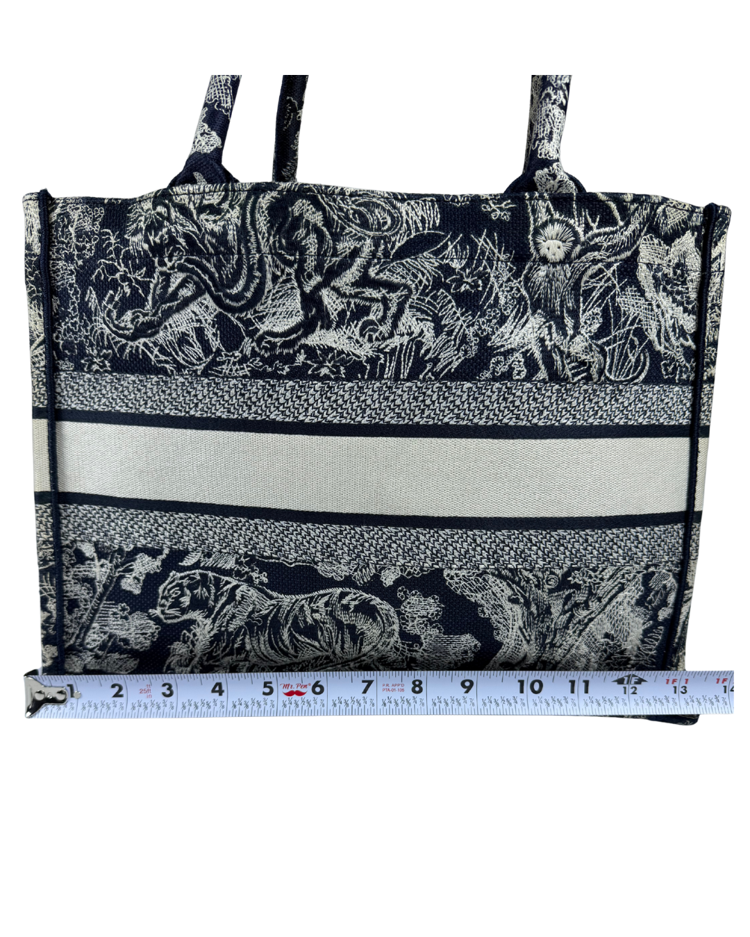 A black and white patterned tote bag with a horizontal cream stripe, shown with a measuring tape ruler along the bottom edge to indicate size.