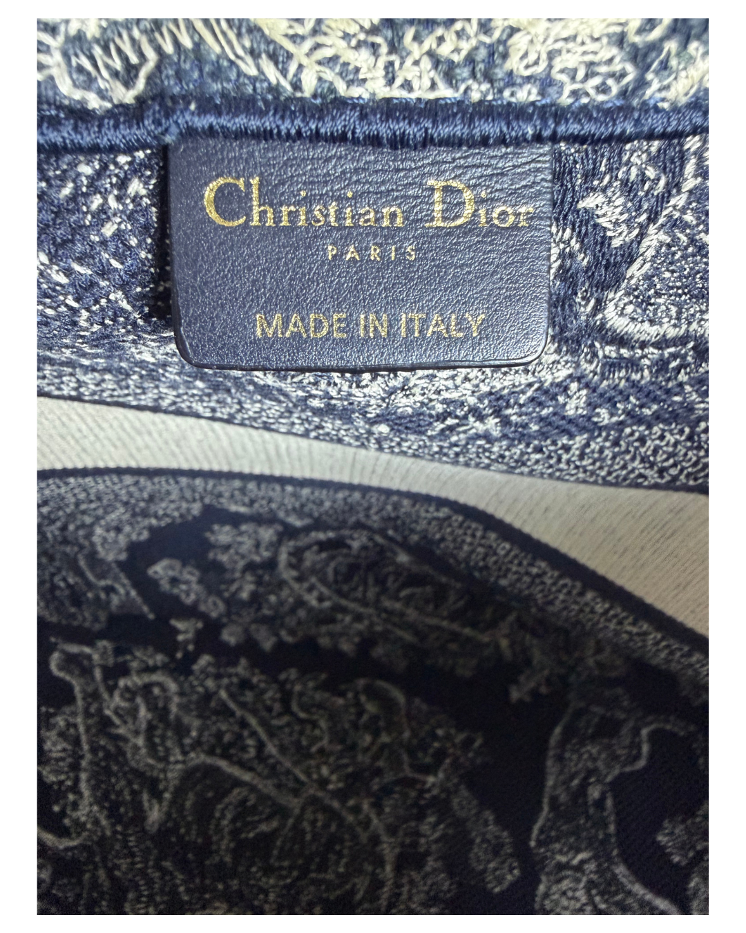 Close-up of a Christian Dior Paris label stitched inside a navy blue and beige patterned fabric book tote.