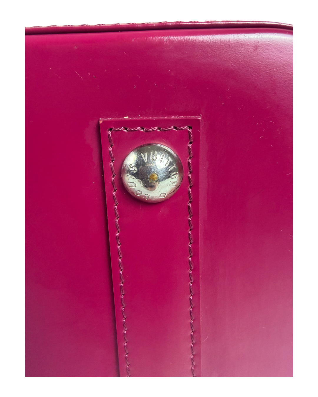 A close-up of a bright magenta pink leather bag featuring a silver-tone metal snap button with the brand name 'LOUIS VUITTON' engraved on it.