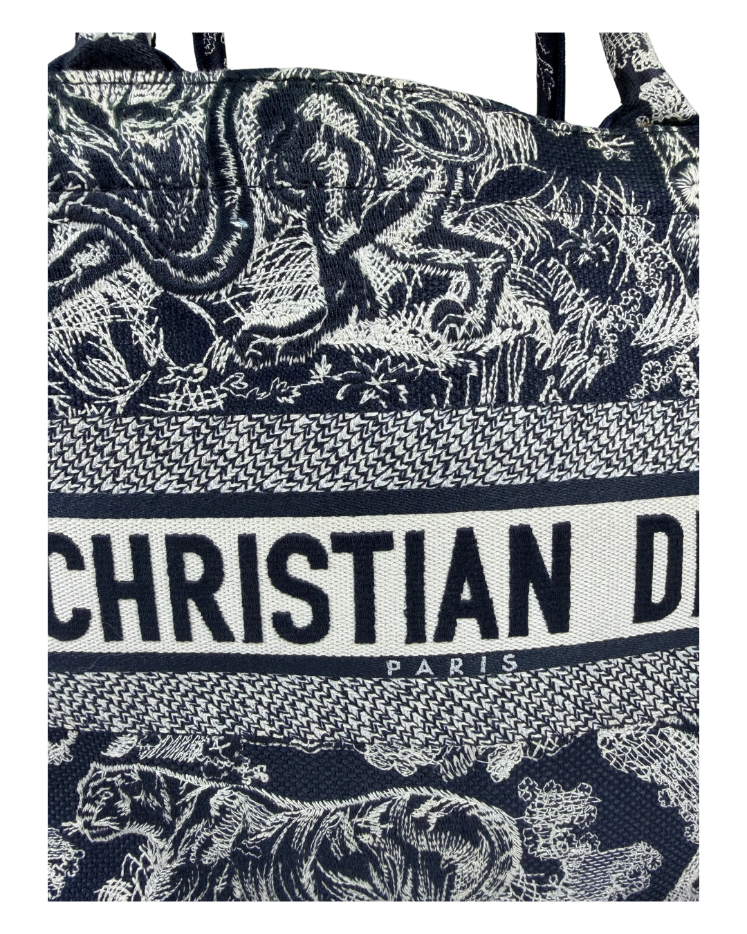 A close-up of a Christian Dior canvas tote bag featuring a navy blue and off-white patterned design with illustrations of lions and the brand name 'CHRISTIAN DIOR PARIS' printed across the center.