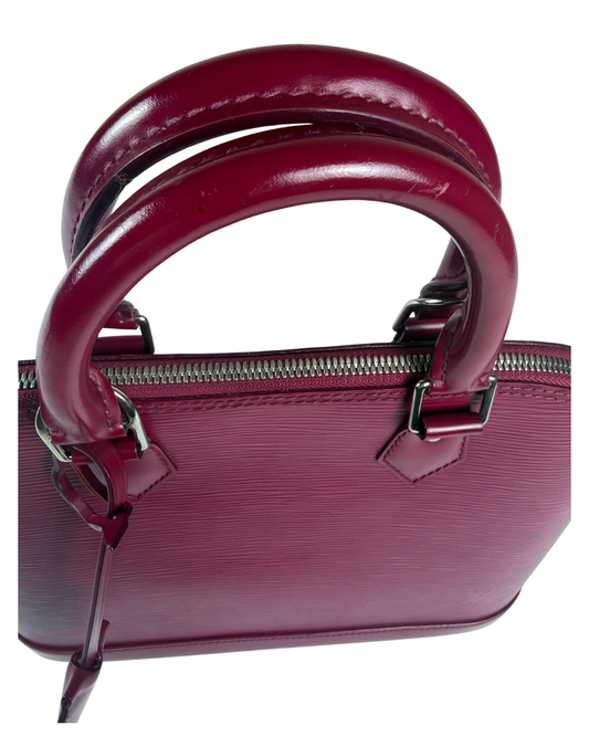 A close-up of a structured handbag in deep burgundy Epi leather, featuring double top handles and silver-tone hardware, set against a plain white background.