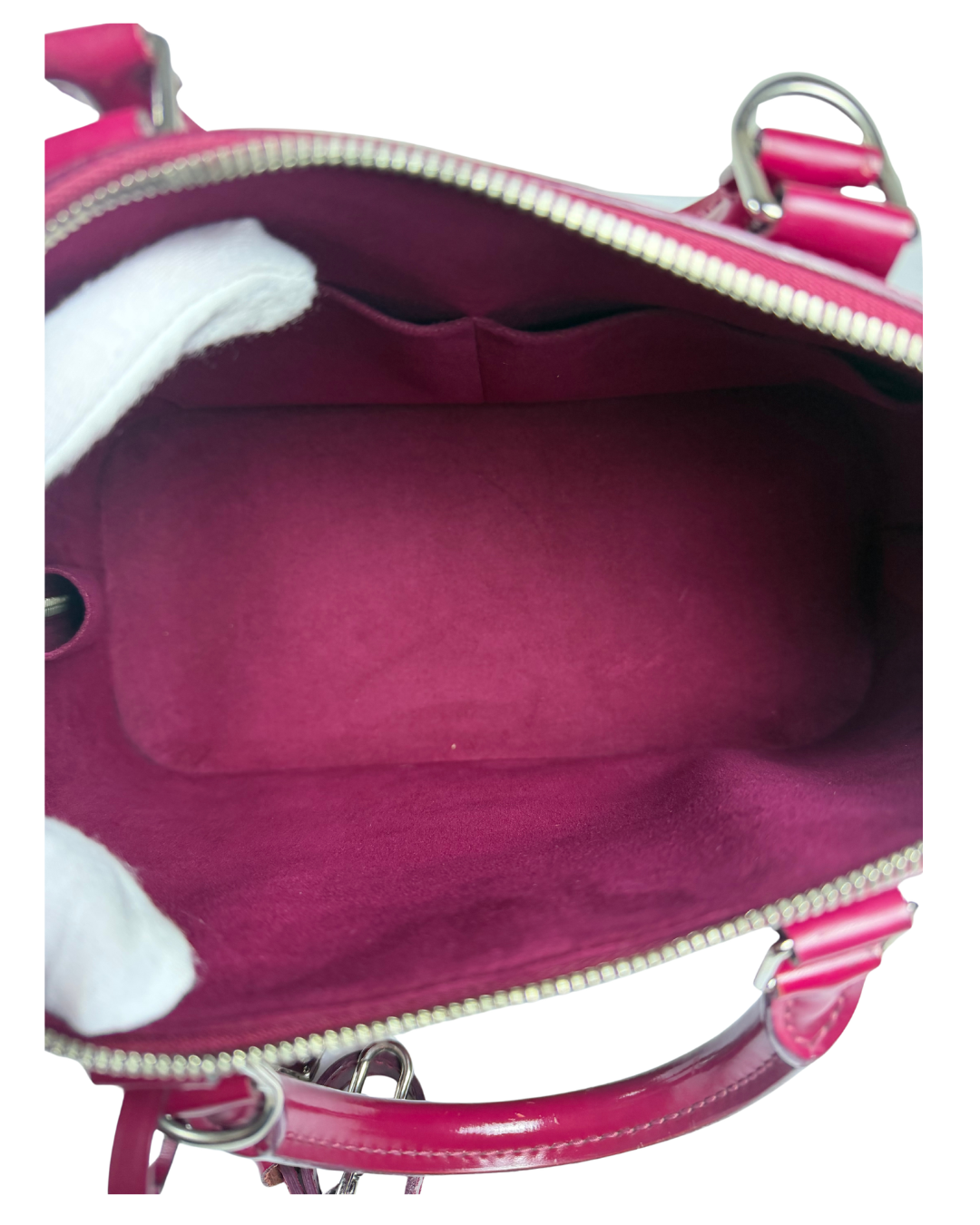 A close-up view of a handbag's interior, showing a deep magenta velvet-lined compartment with a silver zipper, and a matching pink patent leather handle. 
