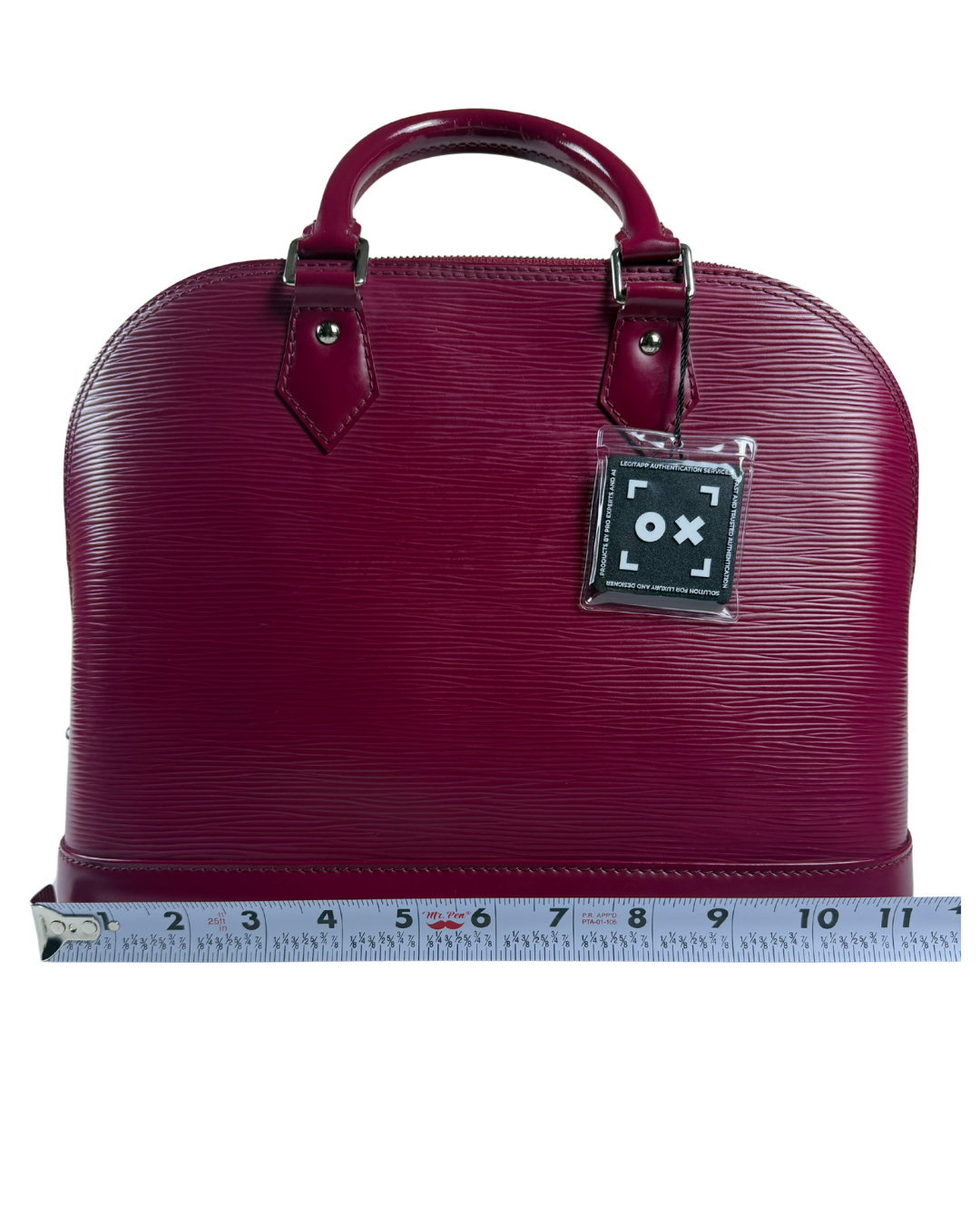 A burgundy Louis Vuitton Alma BB handbag with a textured Epi leather finish, shown with a measuring tape along the bottom to indicate its height.