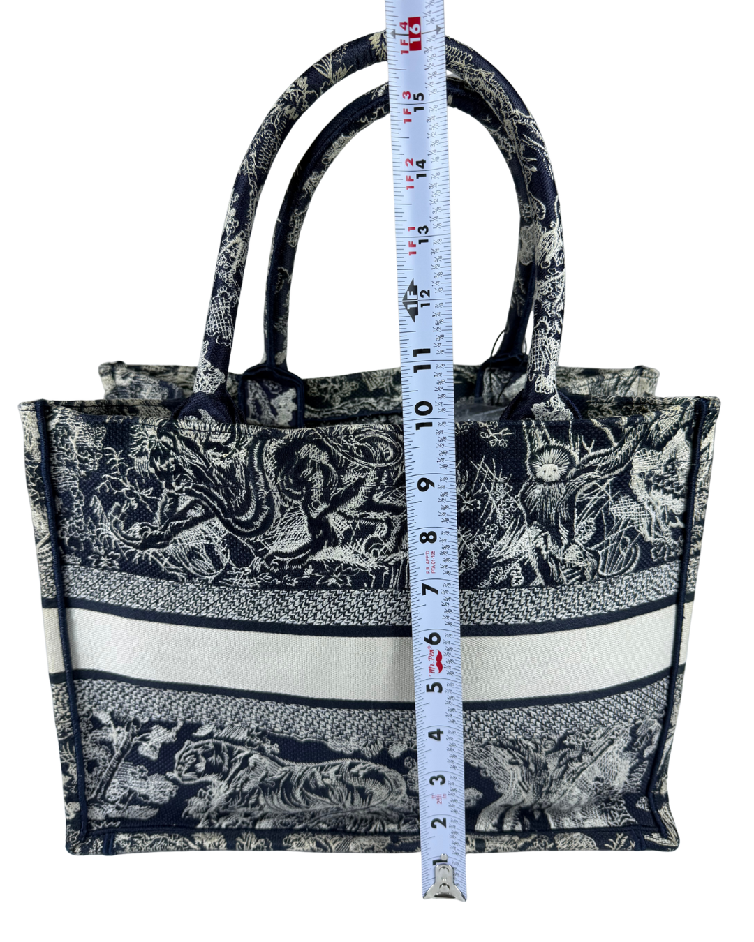 A black and white patterned tote bag with a horizontal cream stripe, shown with a US measuring tape vertically aligned in front of it to indicate size.