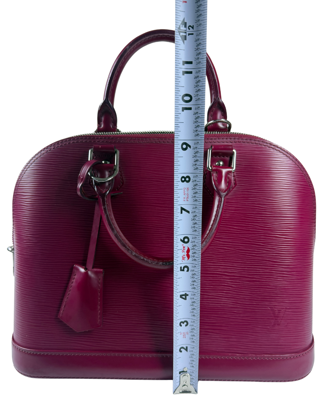 A burgundy Louis Vuitton Alma handbag with a vertical measuring tape overlaid in the center to show its height, photographed against a plain white background.