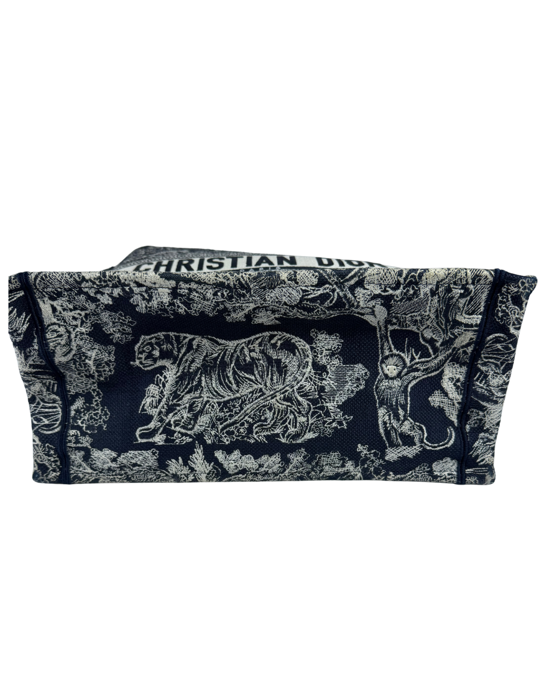 A Christian Dior handbag bottom view with a dark navy blue and white toile de Jouy pattern featuring a tiger and floral motifs, shown against a plain white background.