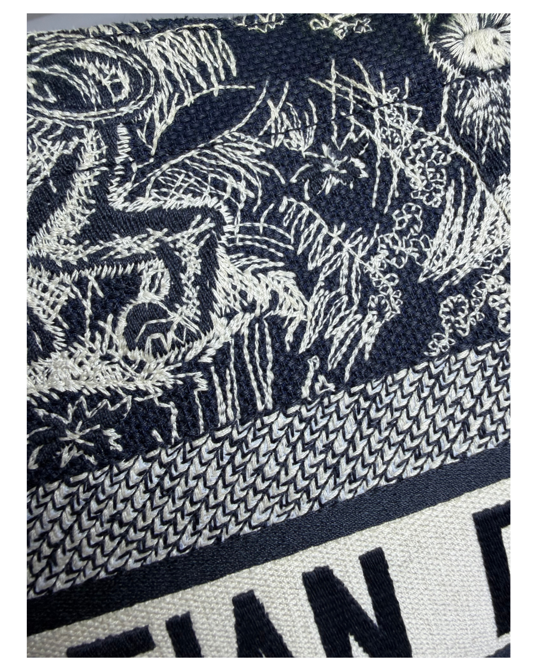 Close-up of a woven textile with a dark navy and off-white abstract botanical or floral pattern, plus a textured band and partial bold lettering at the bottom.