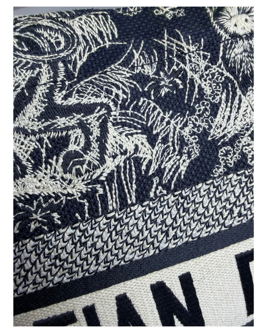 Close-up of a woven textile with a dark navy and off-white abstract botanical or floral pattern, plus a textured band and partial bold lettering at the bottom.