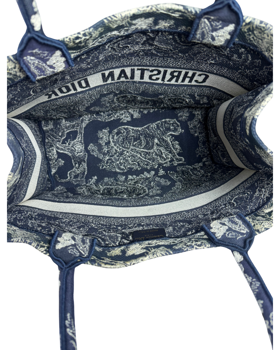 Open view of a Christian Dior tote bag showing the interior lining with a navy blue and white patterned print, a white band with black 'CHRISTIAN DIOR' text, and matching fabric handles.